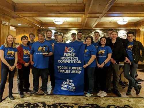 Team stands holding banner that reads "Woodie Flowers Finalist Award" 