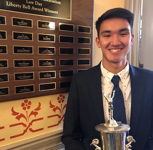 Student holds trophy while standing next to plaques showing the names of previous Law Day winners